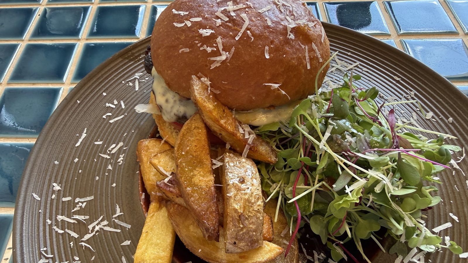 真上から見た一皿。パルメザンをふったバンズのハンバーガーに、皮つきのくし切りポテトとベビーリーフが添えられている