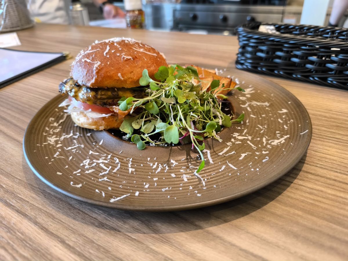 木のカウンター席に置かれた、ベビーリーフを添えたハンバーガーの皿。奥にオープンキッチンが見える