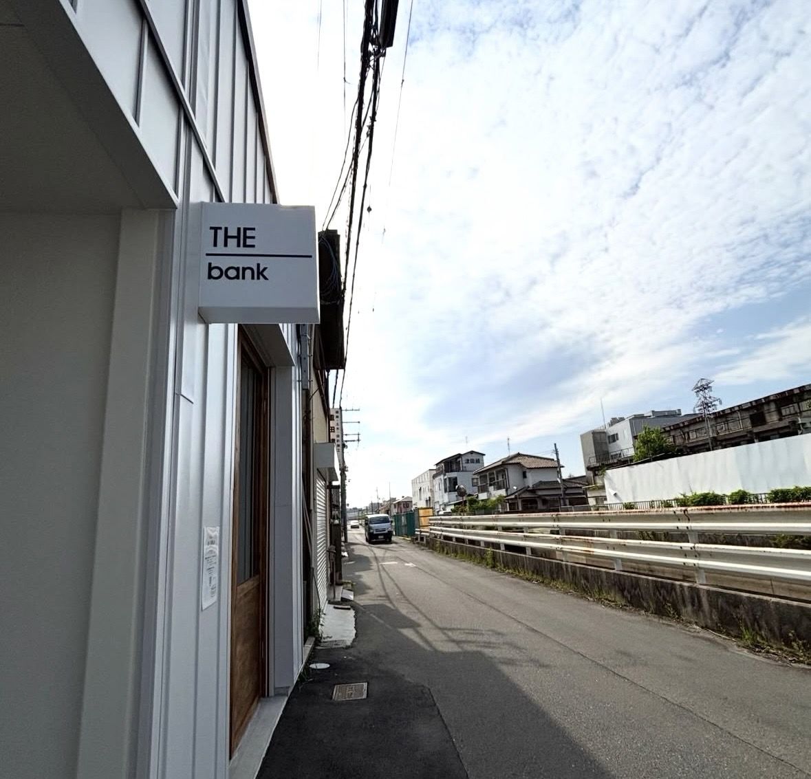 白い外壁の建物に突き出した、白地に黒文字で THE bank と書かれた看板